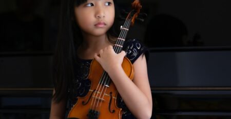 upper-section-portrait-of-an-asian-adorable-little-girl-sitting-in-front-of-piano-holding-a-violin-in_t20_pRLaWd